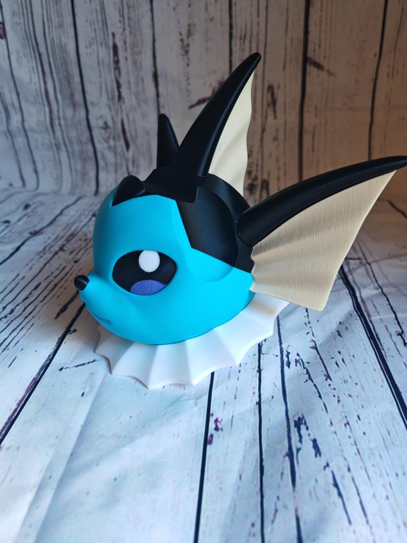 May include: A blue and black 3D printed figurine of a Pokemon character with a white collar. The figurine is posed with its head tilted to the side.