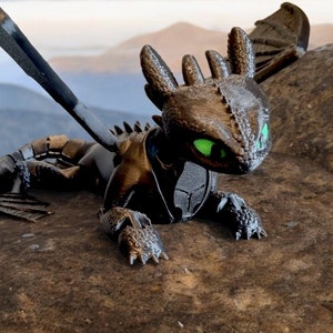 K&ouml;nnte beinhalten: Eine schwarze und gr&uuml;ne Drachenfigur mit einer strukturierten Oberfl&auml;che. Der Drache hat einen langen Schwanz und Fl&uuml;gel, und seine Augen sind gr&uuml;n. Die Figur sitzt auf einem Felsen.