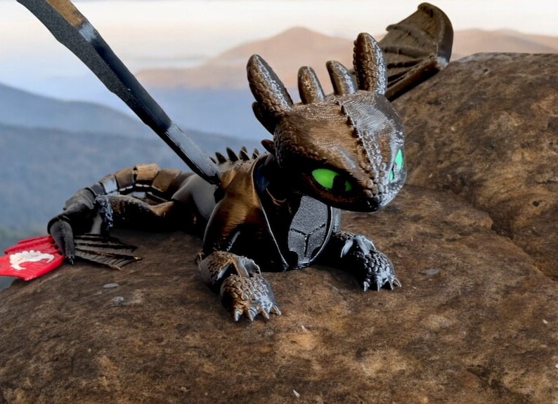 K&ouml;nnte beinhalten: Eine schwarze und gr&uuml;ne Drachenfigur mit einer strukturierten Oberfl&auml;che. Der Drache hat einen langen Schwanz und Fl&uuml;gel, und seine Augen sind gr&uuml;n. Die Figur sitzt auf einem Felsen.
