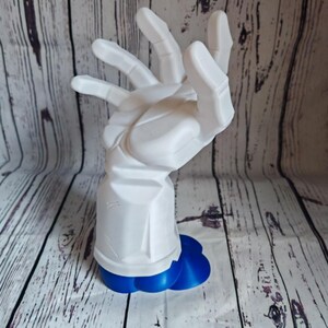 K&ouml;nnte beinhalten: Eine wei&szlig;e, 3D-gedruckte Handskulptur mit einem blauen Sockel. Die Hand ist mit ausgestreckten und leicht gekr&uuml;mmten Fingern positioniert. Die Skulptur ist ein einzigartiges und modernes Kunstwerk.