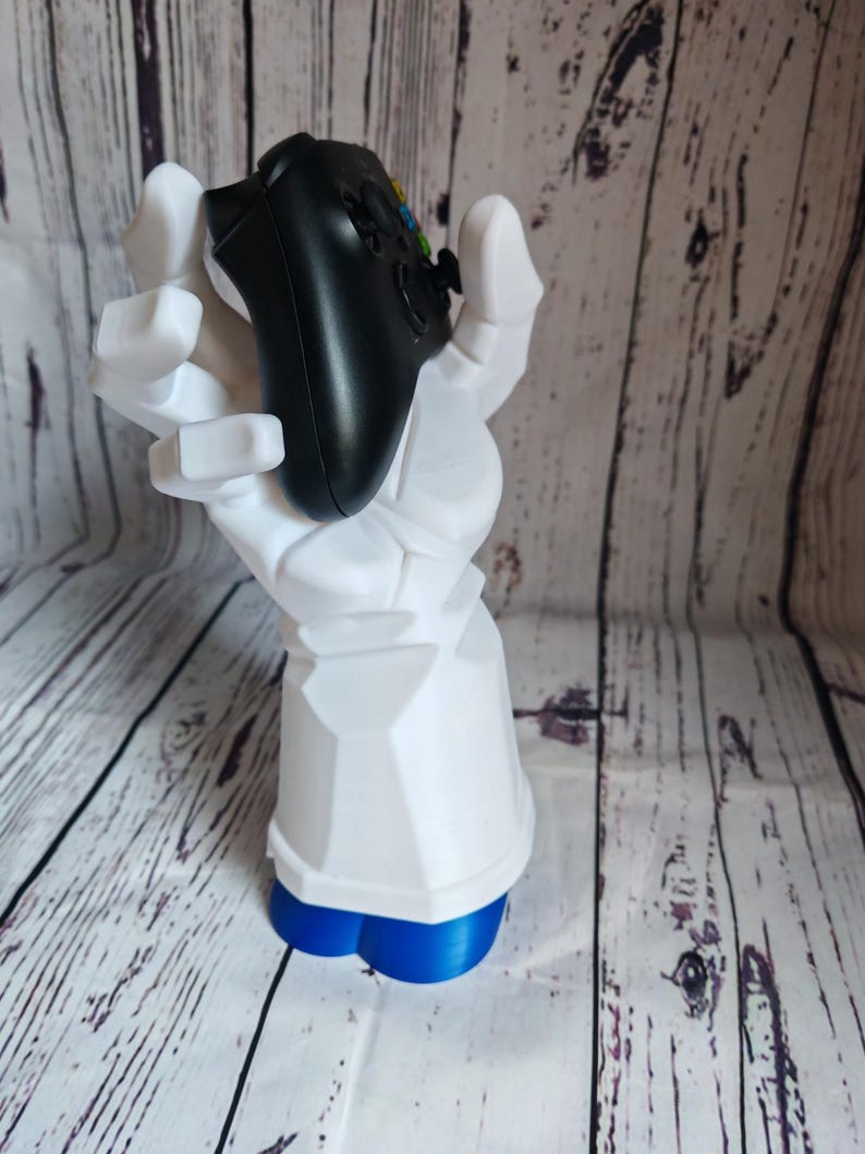 K&ouml;nnte beinhalten: Eine wei&szlig;e, im 3D-Druck hergestellte Hand h&auml;lt einen schwarzen Videospiel-Controller. Die Hand steht auf einem blauen Sockel.
