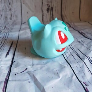 Puede incluir: Un juguete de pl&aacute;stico azul claro de un personaje de Pokemon con ojos rojos y marcas verdes. El juguete est&aacute; en vista de perfil.
