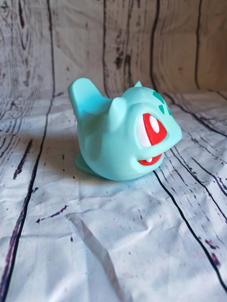 Puede incluir: Un juguete de pl&aacute;stico azul claro de un personaje de Pokemon con ojos rojos y marcas verdes. El juguete est&aacute; en vista de perfil.
