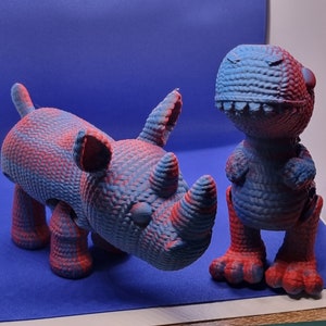 May include: A blue and red rhinoceros and a blue and red dinosaur toy. Both toys are made of a textured material and have a cartoonish appearance.