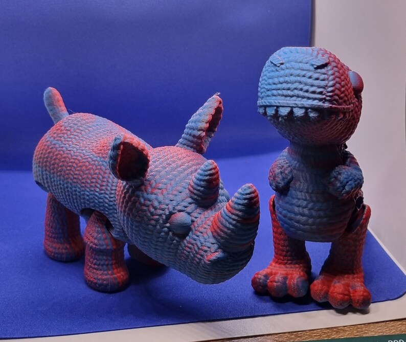 May include: A blue and red rhinoceros and a blue and red dinosaur toy. Both toys are made of a textured material and have a cartoonish appearance.