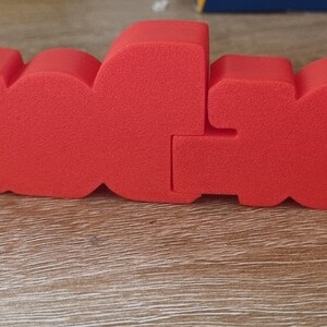 Puede incluir: Letras de espuma roja que deletrean la palabra "LOVE" en un estilo audaz y tridimensional. Las letras est&aacute;n unidas, creando una palabra continua.