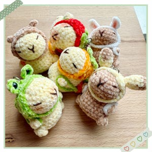 May include: A collection of five plush animal keychains. The keychains are in the shape of sheep, with various hats and accessories, including a frog, bunny, and bear. The keychains are made of soft, textured yarn in shades of cream, brown, green, orange, and red.