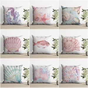 Può includere: Nove diverse federe per cuscini con disegni ad acquerello che raffigurano conchiglie, stelle marine, cavallucci marini e coralli. I cuscini sono tutti bianchi con uno sfondo rosa chiaro, blu o verde.