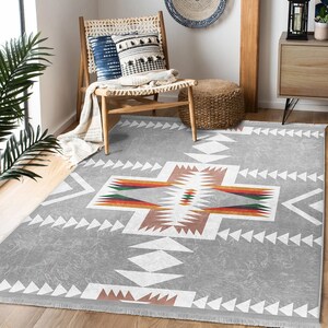 May include: A gray area rug with a white, brown, and red geometric pattern. The rug has a fringe border.
