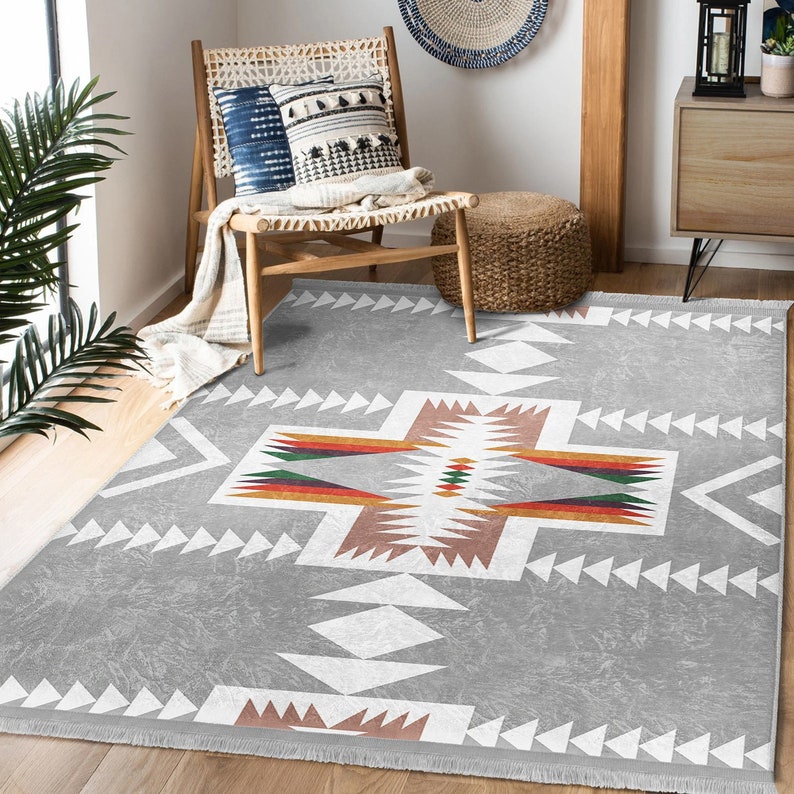 May include: A gray area rug with a white, brown, and red geometric pattern. The rug has a fringe border.