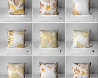 May include: Nine square decorative throw pillows with various leaf designs in gold, brown, and white. The pillows feature different leaf patterns, including ferns and autumn leaves, creating a nature-inspired theme. The pillows are square and appear to be made of a soft fabric.
