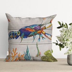 May include: A colorful pillow featuring a blue, green, orange, and purple lobster on a white wood plank background. The lobster is surrounded by coral and seaweed.