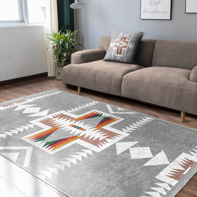May include: A gray area rug with a white geometric pattern and colorful accents. The rug has a Southwestern design with a cross shape in the center.