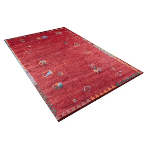 May include: Red rug with a geometric pattern in shades of blue, yellow, and green. The rug has a distressed look and is made of wool.