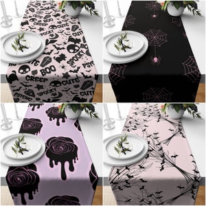 May include: Four different Halloween table runners. The first runner is pink with black bats, skulls, and text that says "Boo", "Creepy", "Spooky", "Cute", and "Psycho". The second runner is black with pink spiderwebs and spiders. The third runner is pink with black dripping roses. The fourth runner is pink with black bats and branches.