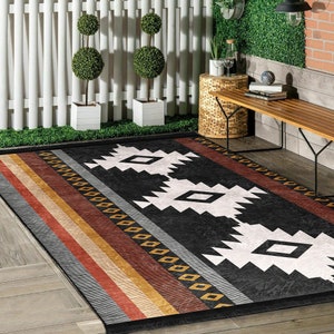 May include: Black and white geometric patterned rug with red, gold, and beige stripes. The rug is laid out on a wooden floor in an outdoor patio setting.