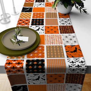 May include: A Halloween-themed table runner with a patchwork design featuring orange, black and white squares. Each square has a different pattern, including bats, pumpkins, spiders and ghoulish faces.