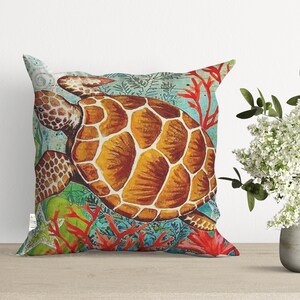 May include: A colorful throw pillow featuring a detailed illustration of a sea turtle swimming through coral reefs. The turtle is brown with a yellow shell and is surrounded by red and green coral.