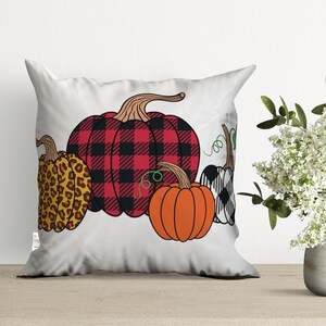 May include: A white pillow with a design of four pumpkins. The pumpkins are in a row and are different colors and patterns. The pumpkin on the left is brown and orange with a leopard print. The next pumpkin is red and black with a plaid pattern. The third pumpkin is orange and the last pumpkin is black and white with a checkered pattern.