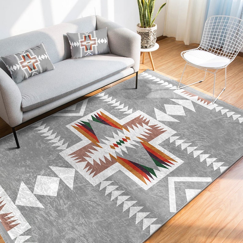 May include: A gray area rug with a geometric pattern in white, brown, orange, red, and green. The pattern features a large central diamond shape with smaller triangles and zigzags.