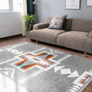May include: A gray area rug with a white geometric pattern and colorful accents. The rug has a Southwestern design with a cross-shaped pattern in the center.