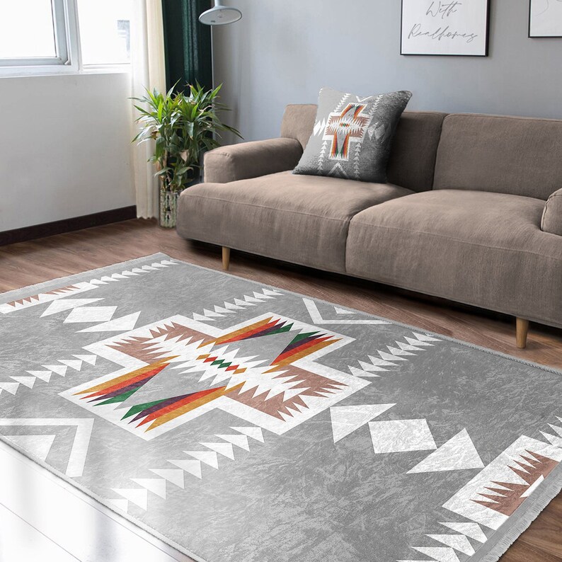 May include: A gray area rug with a white geometric pattern and colorful accents. The rug has a Southwestern design with a cross-shaped pattern in the center.