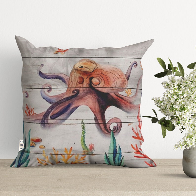 May include: A watercolor pillow featuring a colorful octopus with a white woodgrain background. The octopus has pink, orange, and purple tentacles and is surrounded by coral and seaweed.
