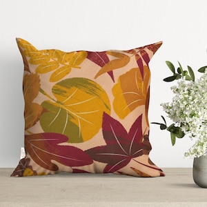 May include: A square throw pillow with a beige background and a pattern of stylized leaves in shades of red, orange, yellow, and green.