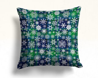 May include: A green and blue throw pillow with a snowflake pattern. The snowflakes are white and are arranged in a plaid pattern.