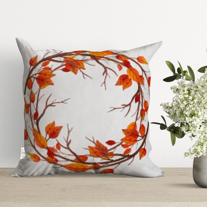 A white throw pillow with a circular design of orange and brown leaves on branches. The design is centered on the pillow.