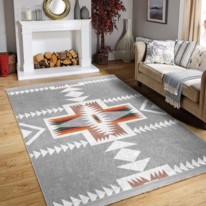 May include: A gray area rug with a white geometric pattern. The pattern features a large cross shape with smaller triangles and diamonds. The rug has a fringe border.