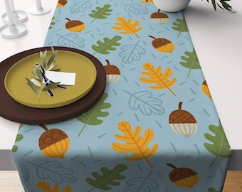 May include: A blue table runner with a repeating pattern of green and yellow leaves and brown acorns.