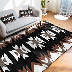 May include: A black and white geometric area rug with brown accents. The rug features a repeating pattern of triangles and zigzags. The rug is shown in a living room setting with a couch and a chair.