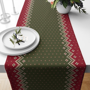 May include: A green and red table runner with a knitted pattern. The runner has a green background with a red and white geometric pattern along the edges.