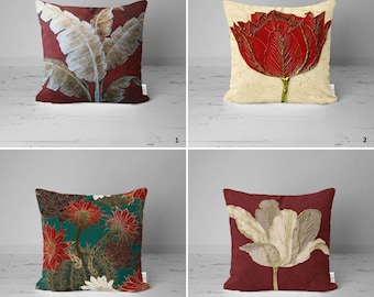 May include: Four decorative throw pillows with floral patterns. The pillows are all red with different floral designs in shades of white, gold, and green. The pillows are arranged in a grid pattern on a white wooden surface.