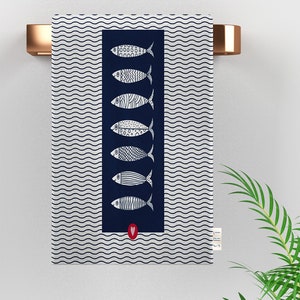 May include: A navy blue kitchen towel with a white wave pattern and a row of white fish with black details. A red heart is in the bottom center of the towel.