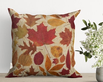 May include: A decorative throw pillow with a beige background and a pattern of colorful autumn leaves in shades of red, orange, yellow, and brown.