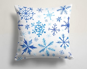 Pode incluir: Almofada quadrada branca com um padrão de flocos de neve azuis em vários tamanhos e designs. Os flocos de neve são em tons de azul claro e escuro, criando um tema de inverno. Para decoração de casa.