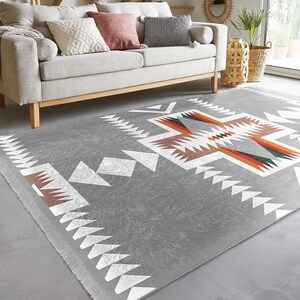 May include: A gray area rug with a white, brown, orange, green, and blue geometric pattern. The rug has a fringe border.
