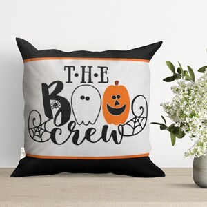 May include: A white pillow with black and orange trim features a Halloween-themed design with the text "THE BOO CREW" and a ghost and pumpkin graphic.