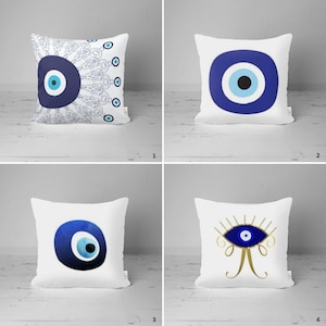 May include: Four white pillow covers with different blue evil eye designs. The first pillow has a blue evil eye with a white center and a blue and white paisley pattern. The second pillow has a simple blue evil eye with a white center. The third pillow has a blue evil eye with a white center and a blue watercolor effect. The fourth pillow has a blue evil eye with a white center and gold eyelashes and a gold design.