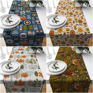 May include: Four table runners with nature-themed designs. One is navy blue with foxes, deer, and owls. Another is beige with orange and yellow flowers. The third is light beige with autumn leaves. The last is olive green with owls and squirrels.