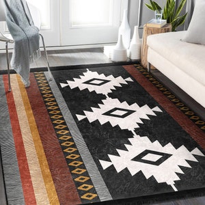 May include: Black and white geometric rug with a southwestern design. The rug has a black background with white diamond shapes and a border of red, orange and yellow stripes.