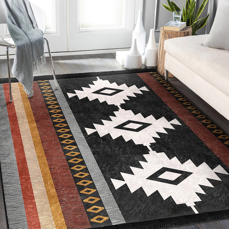 May include: Black and white geometric rug with a southwestern design. The rug has a black background with white diamond shapes and a border of red, orange and yellow stripes.