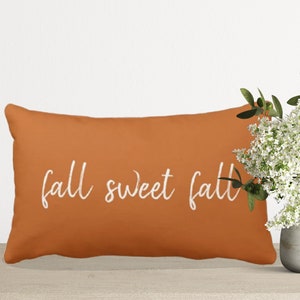 Orange throw pillow with white embroidered text that reads "fall sweet fall".