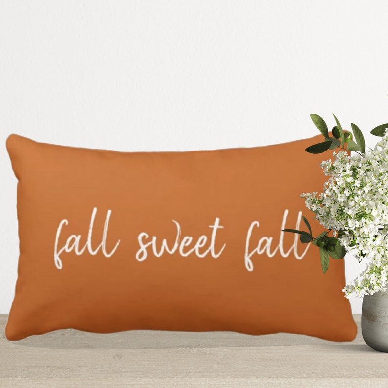 Orange throw pillow with white embroidered text that reads "fall sweet fall".