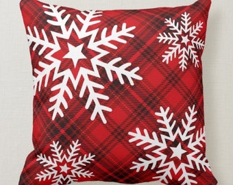 Pode incluir: Almofada quadrada com um padrão xadrez vermelho e desenhos de flocos de neve brancos. A almofada festiva é adequada para a decoração de férias de inverno, adicionando um toque sazonal.