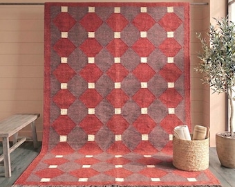 May include: A rectangular area rug featuring a repeating geometric pattern of red and dark gray diamonds separated by small white squares. The rug has a thick red border and a short fringe along the bottom edge, displaying a textured woven surface.