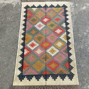Puede incluir: Una alfombra colorida con un patr&oacute;n geom&eacute;trico en tonos de rojo, rosa, amarillo, azul y verde. La alfombra tiene un borde negro y una franja alrededor de los bordes.