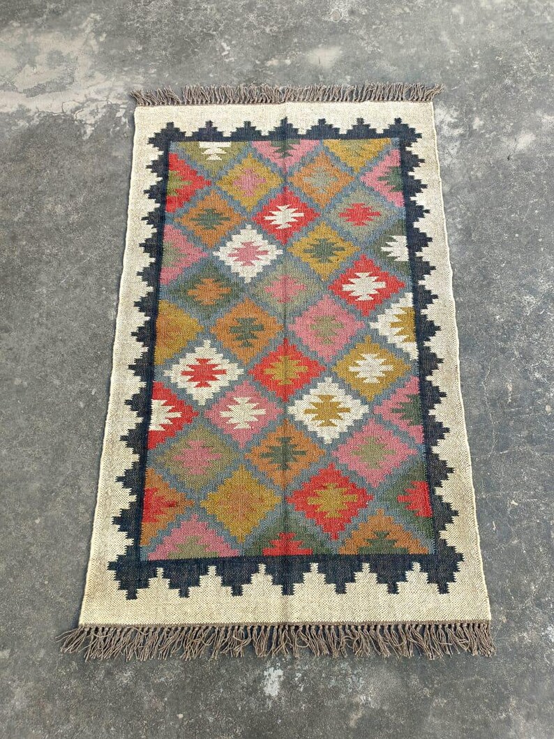 Puede incluir: Una alfombra colorida con un patr&oacute;n geom&eacute;trico en tonos de rojo, rosa, amarillo, azul y verde. La alfombra tiene un borde negro y una franja alrededor de los bordes.